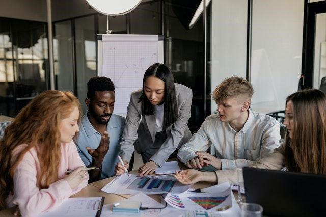 Men and women around a working table with files and charts in front of them.